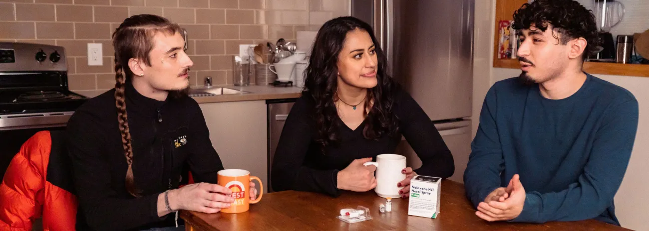 Three friends talking at a kitchen table, drinking coffee.