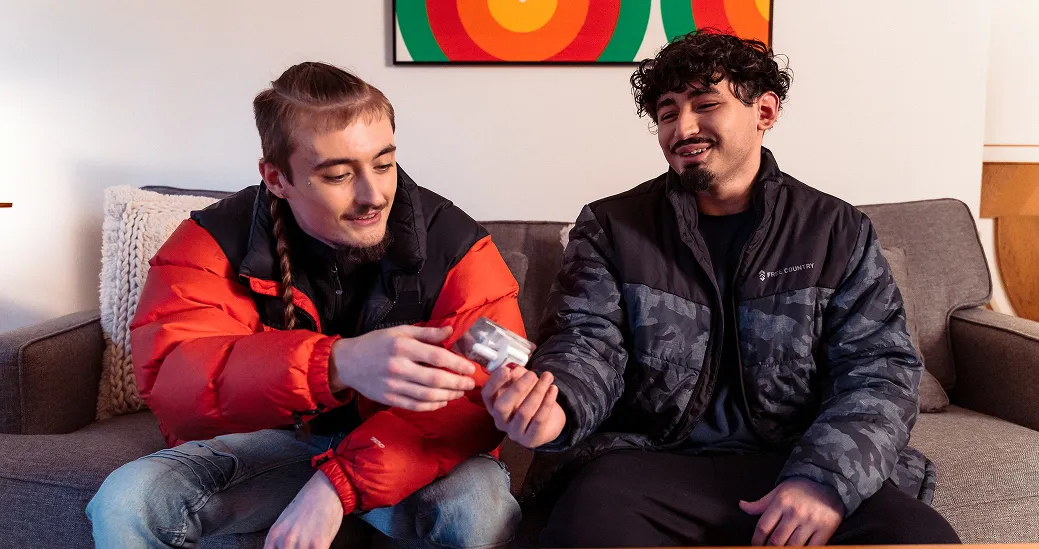Friends sitting on a couch. One handing a naloxone nasal spray to the other.