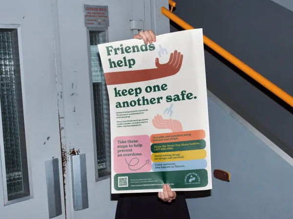 Image of a poster with two hands holding naloxone and the text that friends help keep one another safe