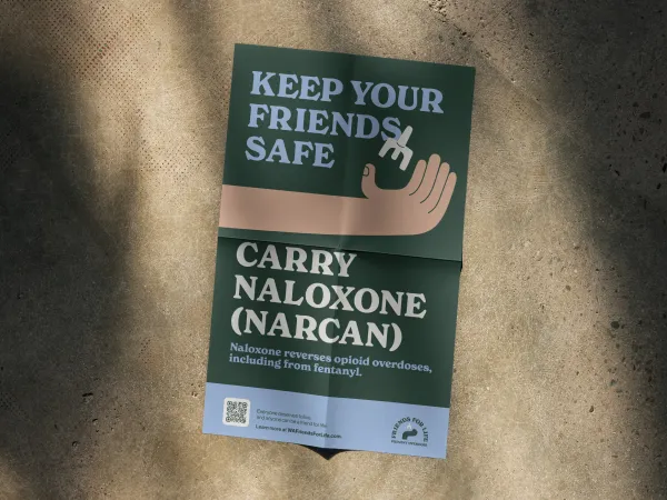 Image of a poster with a dark background and a hand holding Naloxone